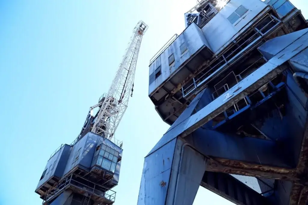 Trump to impose tariffs on Chinese imports 5 Low-angle view of large industrial port cranes against a clear blue sky, representing the heavy lifting equipment used in Jade International's ocean freight and port cargo handling operations.