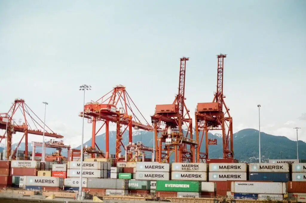 Global Logistics Partnerships Build Stronger Supply Chains 1 Large red gantry cranes and stacked Maersk and Evergreen shipping containers at an international port terminal, representing Jade International's ocean freight forwarding and port operations services.