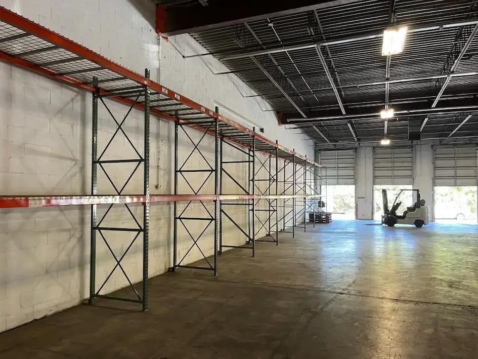 Jade International Expands Warehouse Operations 1 Interior of Jade International's warehouse facility featuring pallet racking, open floor space, loading dock doors, and a forklift, representing their container unloading, storage, and export consolidation services.