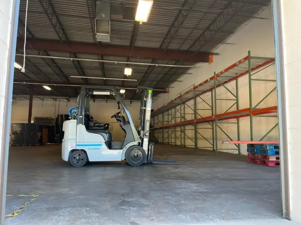 Jade International Expands Warehouse Operations 4 UniCarriers forklift positioned at an open loading dock door inside Jade International's warehouse, with pallet racking and pallets visible, representing their container unloading and warehousing services.