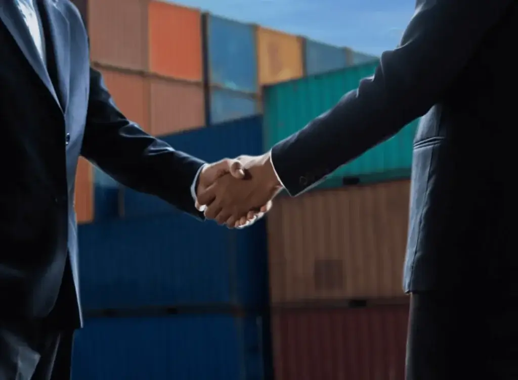 Two business professionals shaking hands in front of stacked shipping containers representing a USMCA trade agreement
