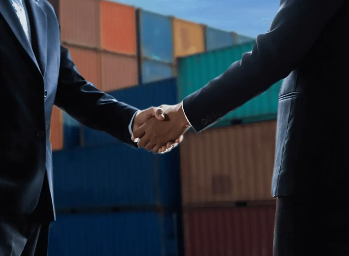 Two business professionals shaking hands in front of stacked shipping containers representing a USMCA trade agreement