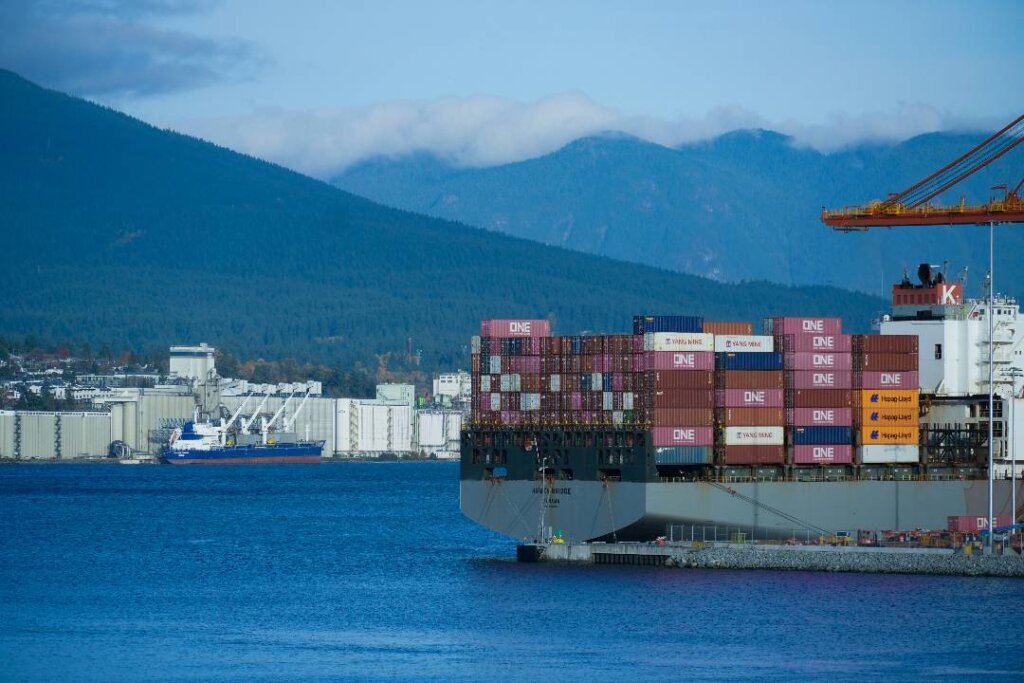Container ship loaded with cargo containers at a port, with mountains in the background.