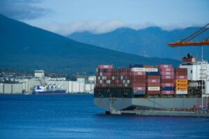 Container ship loaded with cargo containers at a port, with mountains in the background.