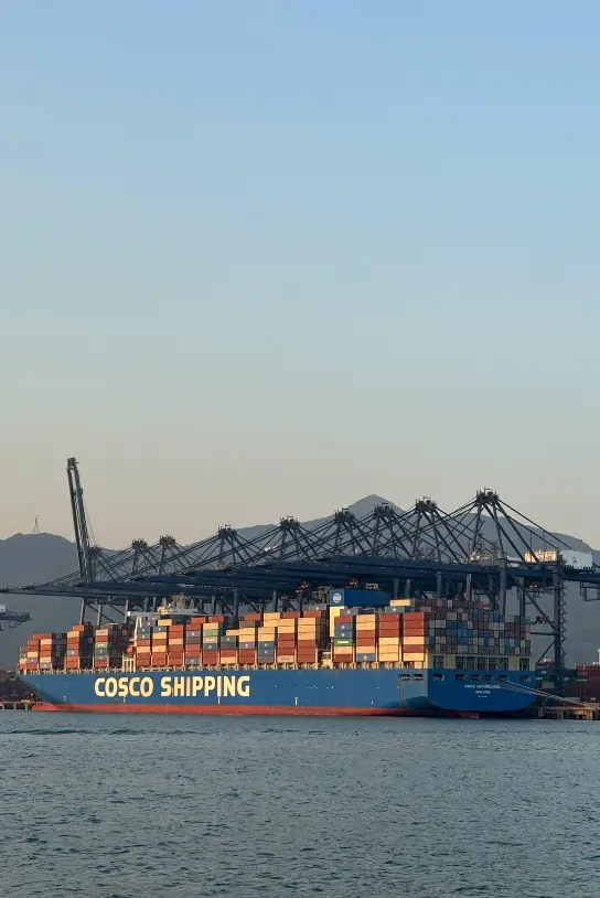 Container ship 'COSCO SHIPPING' loaded with cargo containers at a port, with large gantry cranes in the background