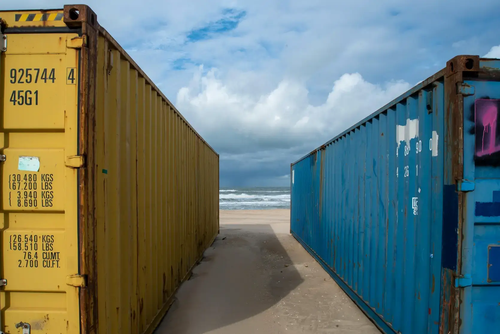 Cargo insurance coverage represented by yellow and blue shipping containers on a sandy shore, with ocean waves visible in the background.