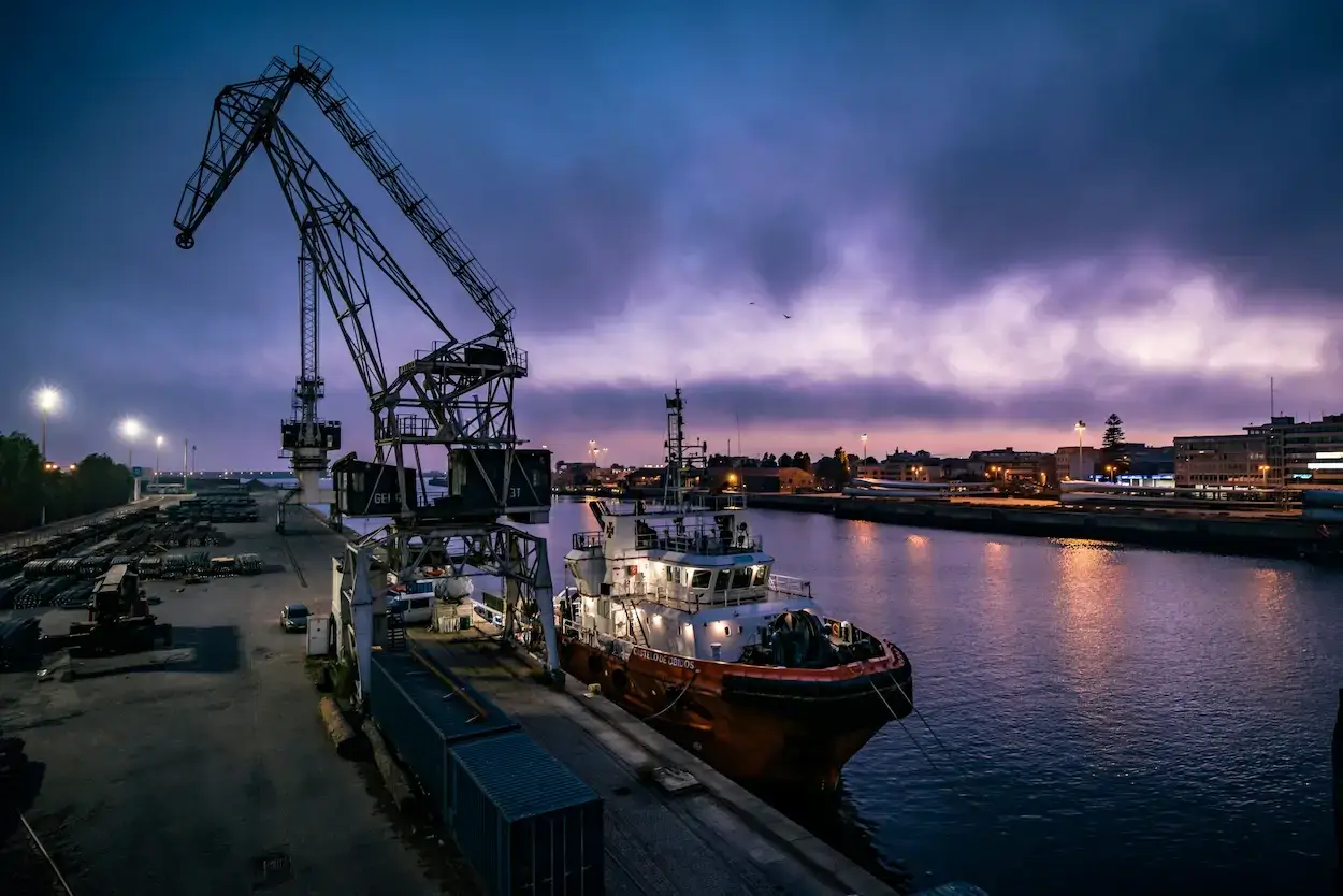 Freight forwarding at a port with cargo vessel and dockside crane at dusk