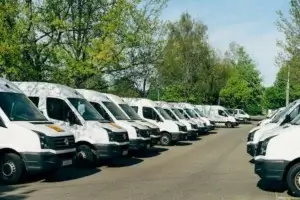 Fleet of white dry van delivery vans parked in a lot surrounded by trees, illustrating commercial freight and last-mile delivery services.