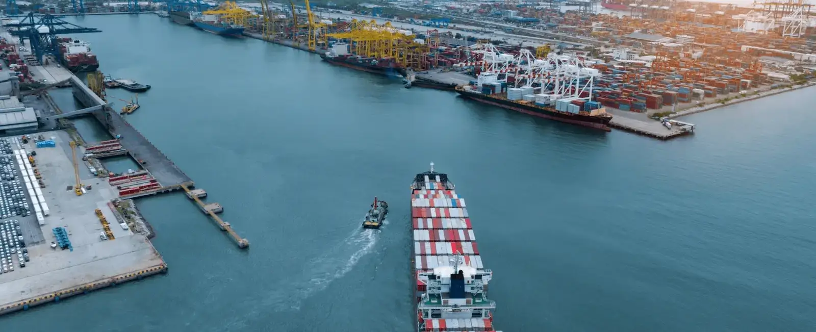 Aerial view of a busy international seaport with container ships, loading cranes, and stacked cargo containers along multiple berths, illustrating Jade International's ocean export and import freight forwarding operations.
