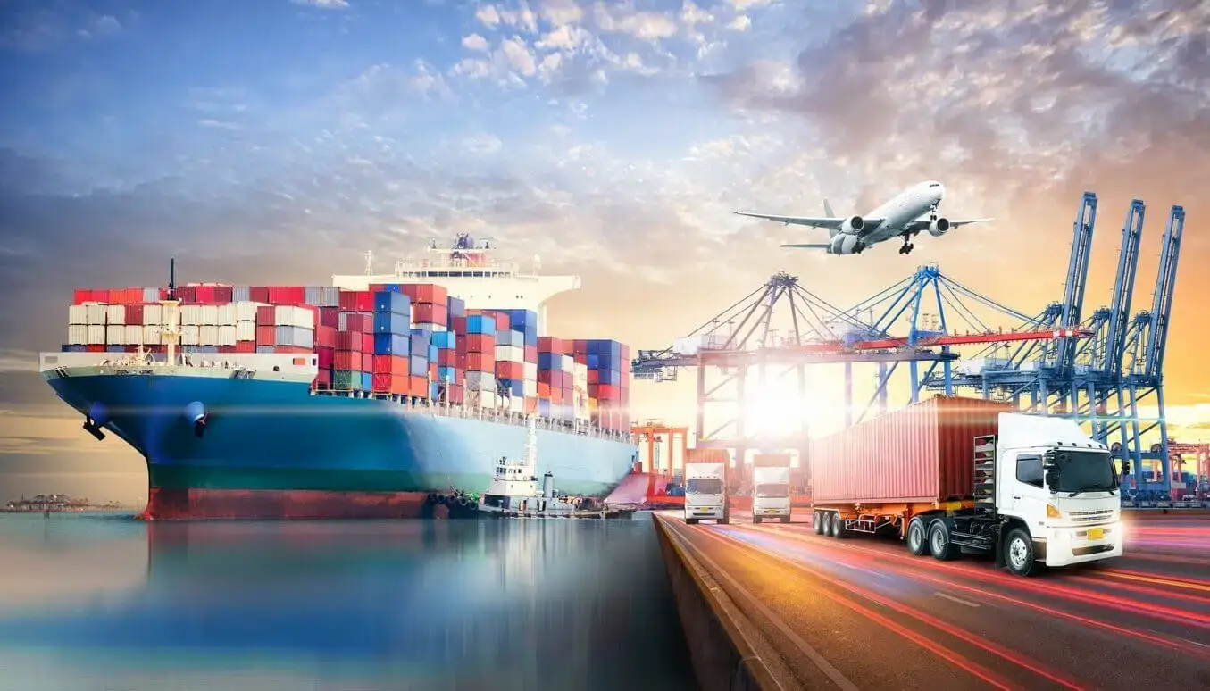 Container ship docked at a port terminal alongside cargo cranes, a container truck on a highway, and a cargo plane overhead, representing Jade International's full-service multimodal freight forwarding by air, ocean, and ground.
