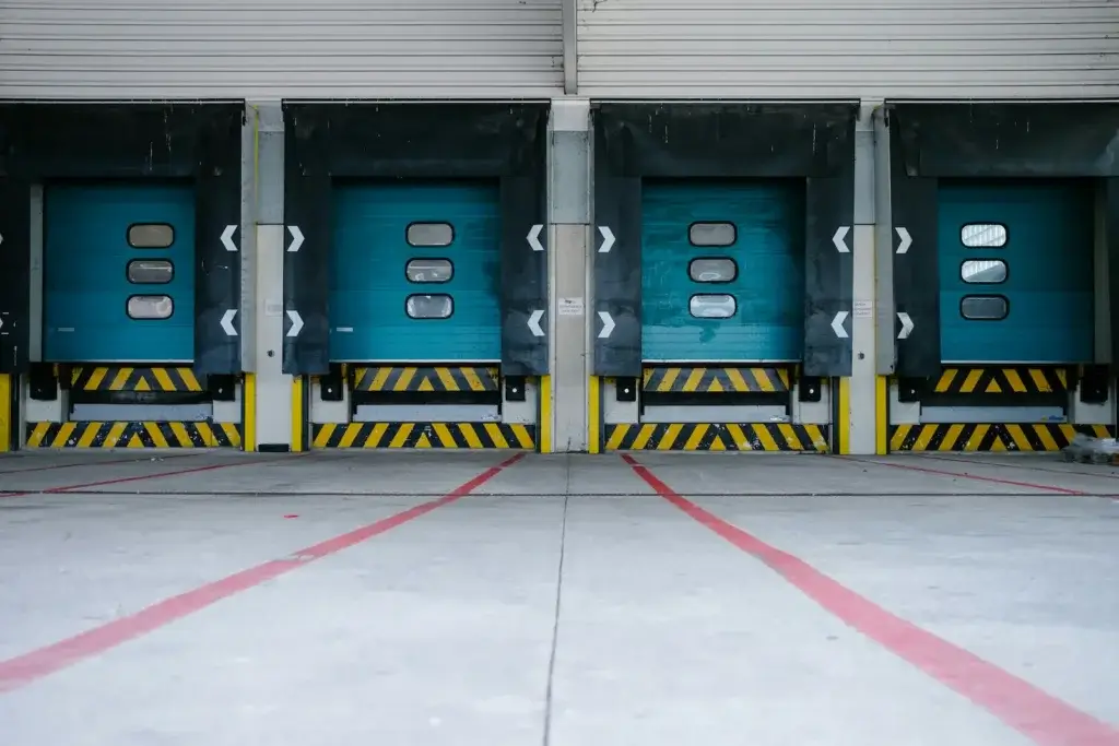 Row of teal loading dock doors with yellow and black safety striping at a cold chain logistics warehouse.