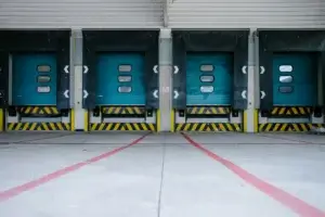 Row of teal loading dock doors with yellow and black safety striping at a cold chain logistics warehouse.