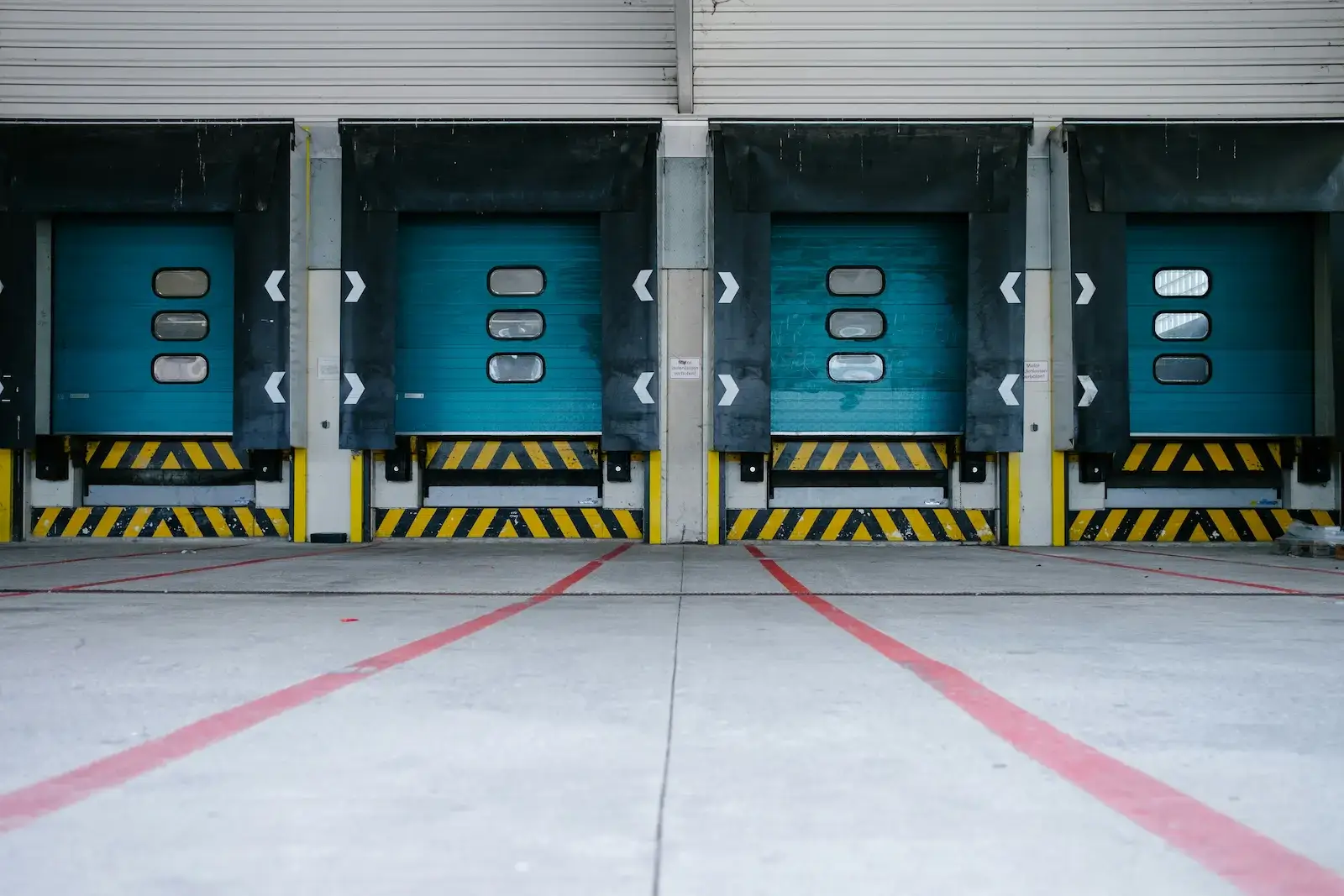 Row of teal loading dock doors with yellow and black safety striping at a cold chain logistics warehouse.