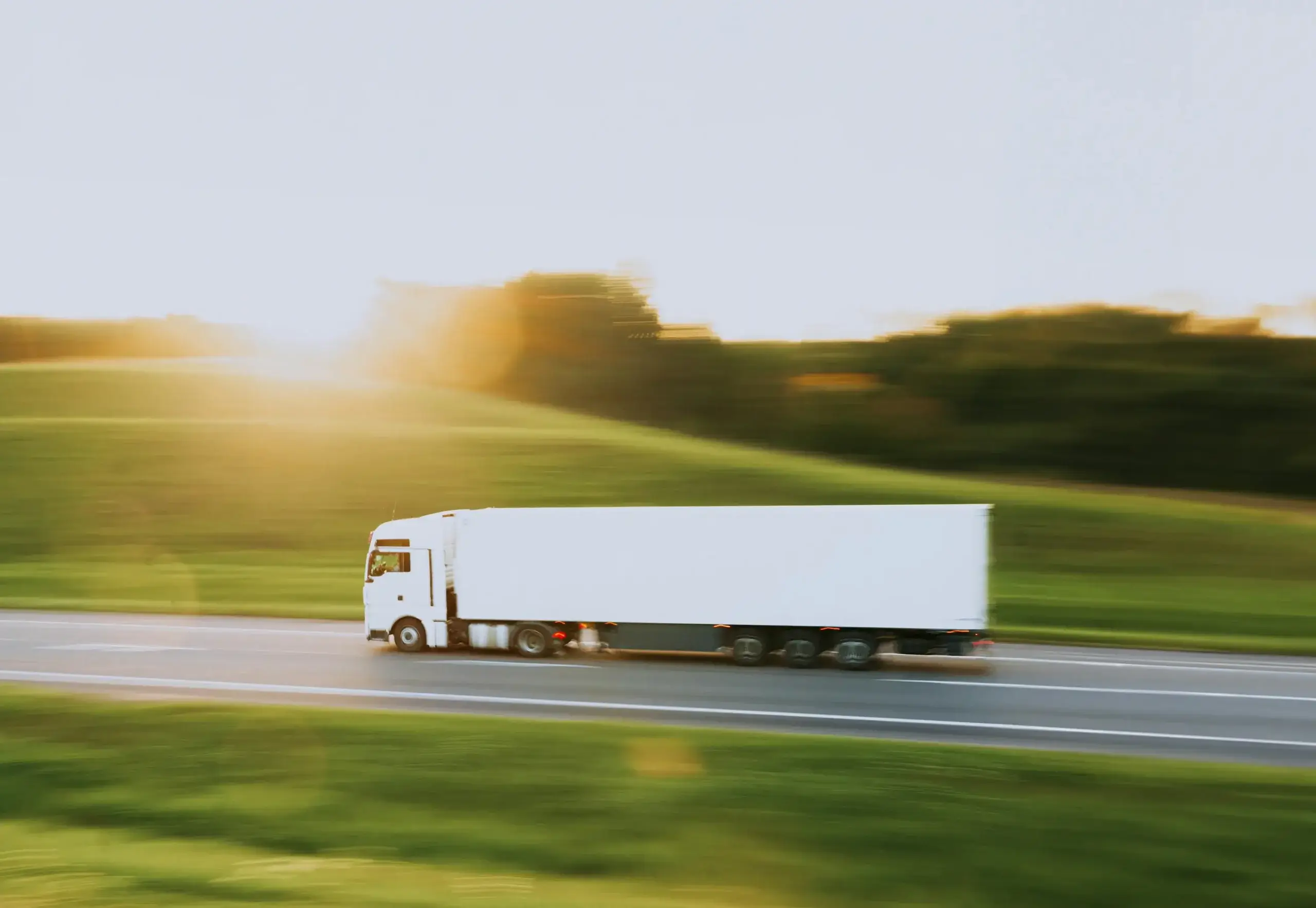 White semi truck with motion blur speeding down a highway at sunset, illustrating expedited freight delivery.