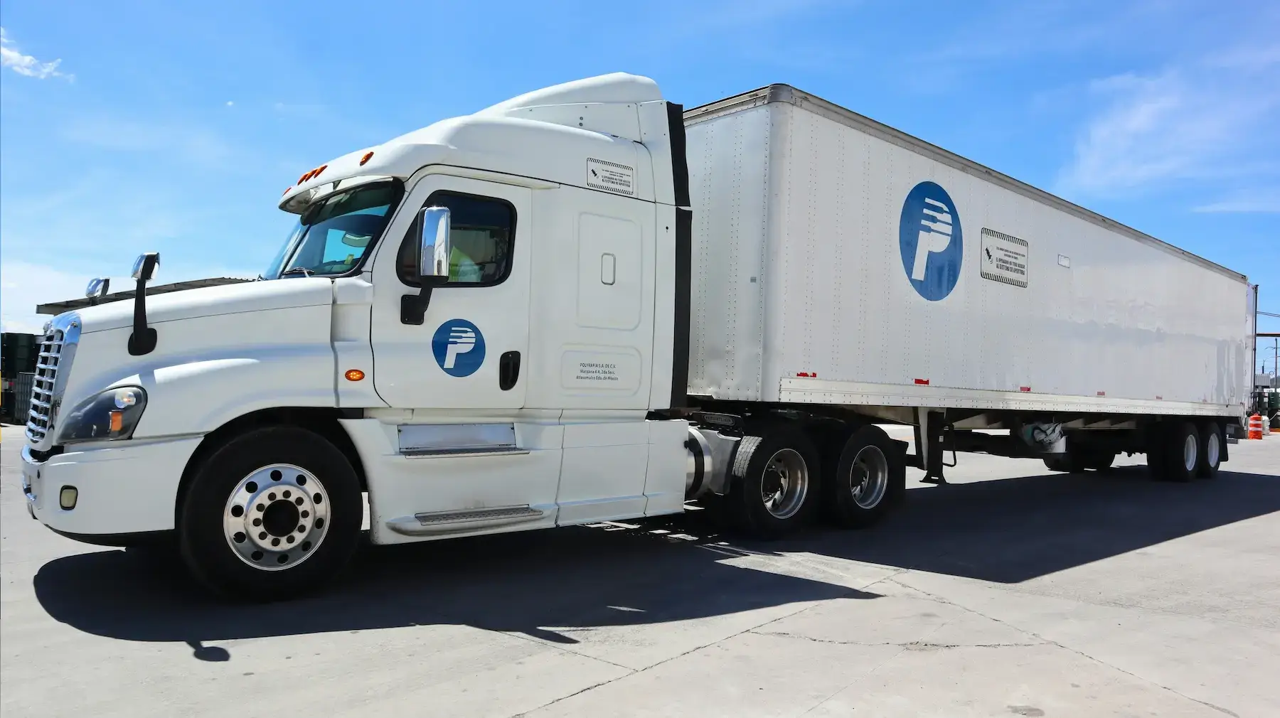 White semi truck with a Polyfrafia branded refrigerated trailer parked in a lot under a clear blue sky, illustrating reefer trucking.