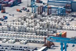 Aerial view of a container freight station with stacked shipping containers, gantry cranes, and trucks moving cargo across the terminal yard.