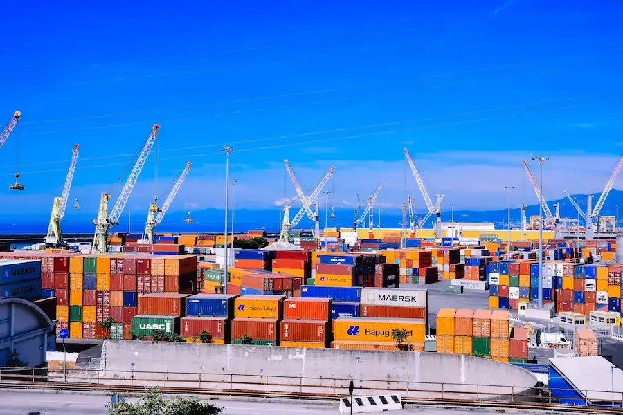 Container ship docked at a busy port with cranes loading shipping containers for freight forwarding