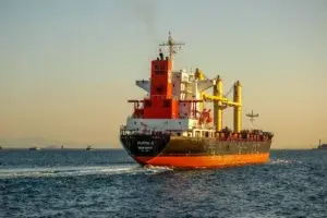 Bulk cargo ship departing port at sunset with tugboats nearby, representing Jade International's ocean freight forwarding services and commitment to on-time delivery.