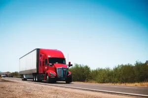 Red semi-trailer truck hauling freight on an open highway under a clear sky